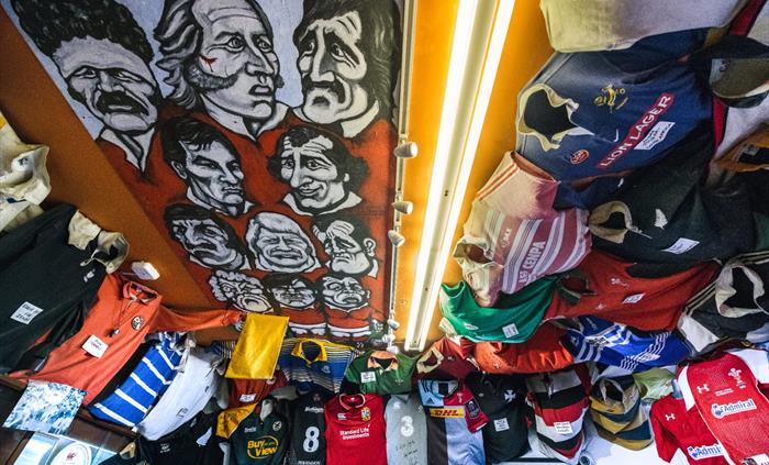 The photo shows a variety of different rugby jerseys attached the ceiling and a painting of Welsh rugby stars.
